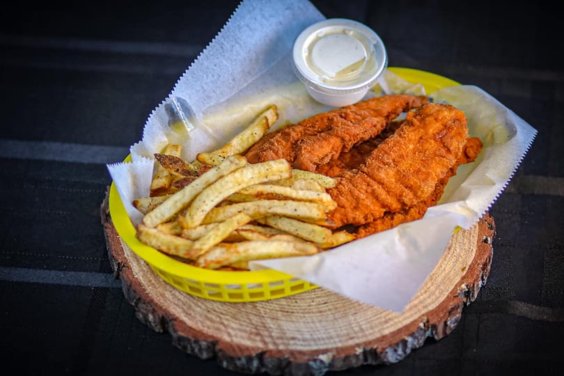 Crispy fried chicken tenders and seasoned french fries in a yellow basket with dipping sauce.