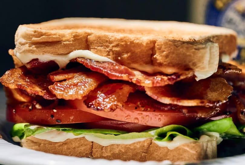 A close-up of a BLT sandwich with crispy bacon, sliced tomatoes, lettuce, and mayonnaise on toast.