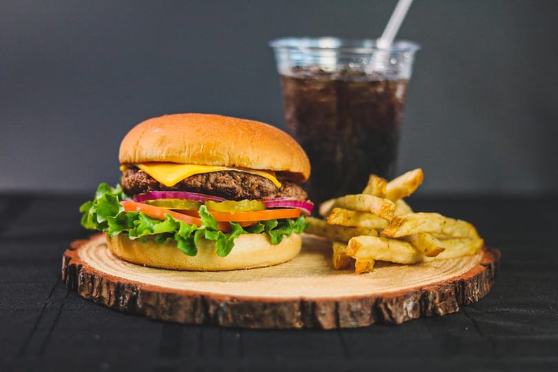 Cheeseburger with lettuce, tomato, onion, and pickles, served with fries and a soda.