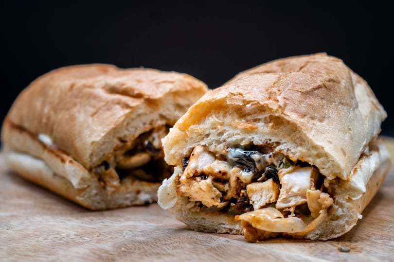 Two halves of a chicken and cheese sub sandwich on a wooden cutting board.