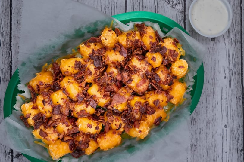 Loaded tater tots with melted cheese and crispy bacon bits in a green basket with ranch.