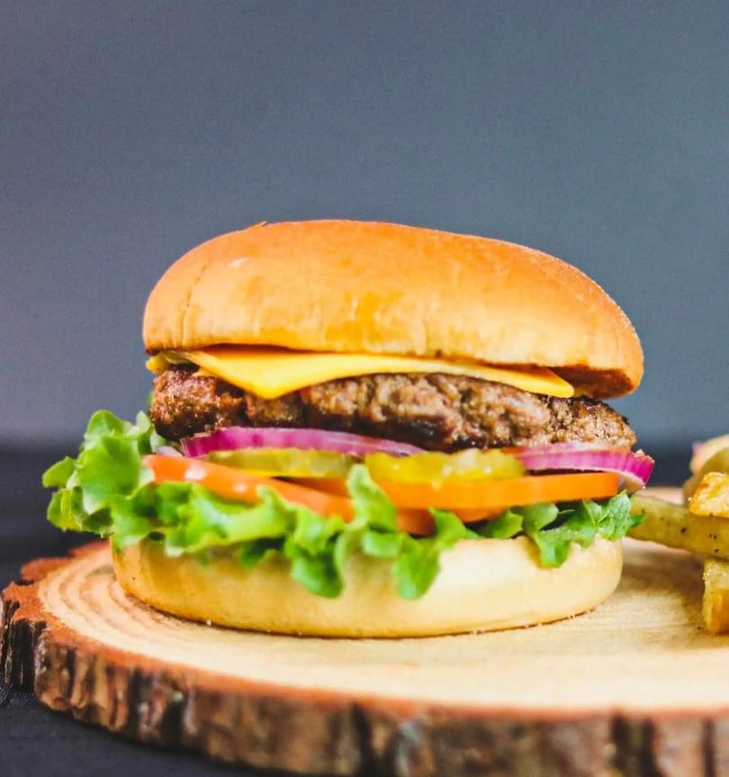 Cheeseburger with lettuce, tomato, onion, and pickles on a wooden board with fries.
